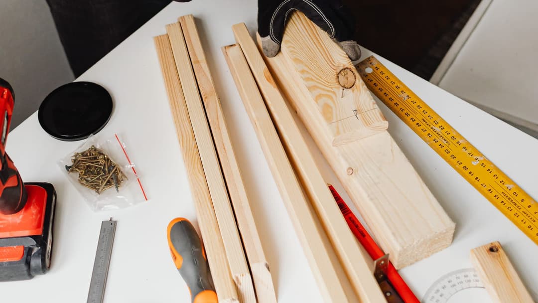 Pine battens, a cordless screwdriver, screws, a tape measure and a screwdriver on a workbench