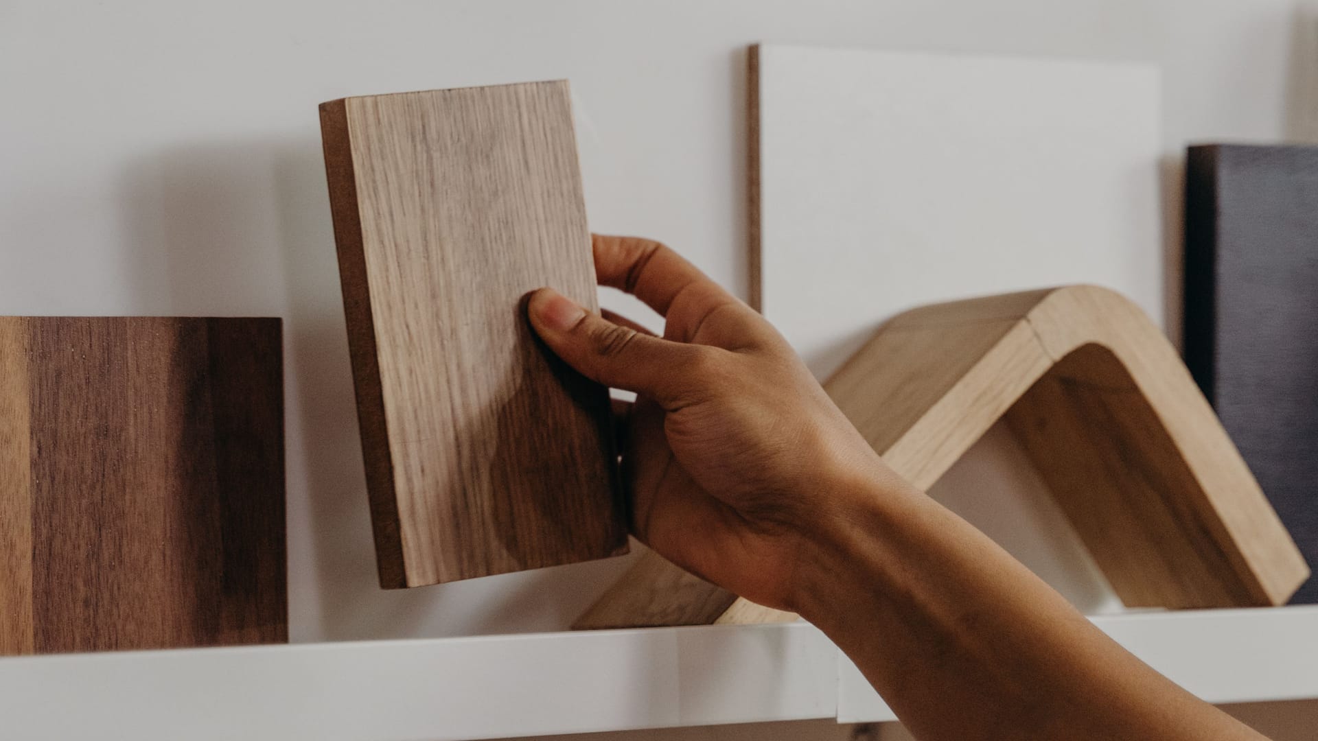 Eine Hand zieht eine Holzdekorprobe aus einem Regal zwischen anderen Plattenmustern