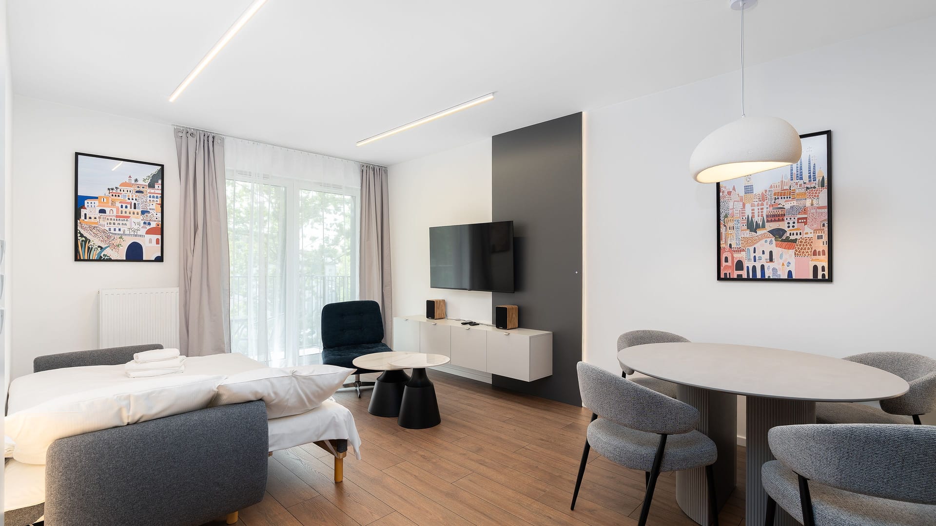 Helle Einzimmerwohnung mit ausgeklapptem Schlafsofa, hängendem TV-Board unter dem Fernseher und rundem Tisch