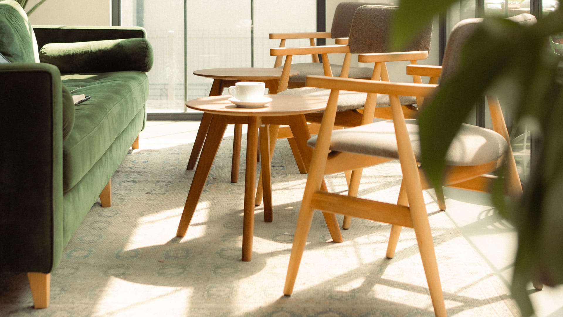 Helles Interieur mit Holzstühlen, runden Beistelltischen und einem grünen Sofa
